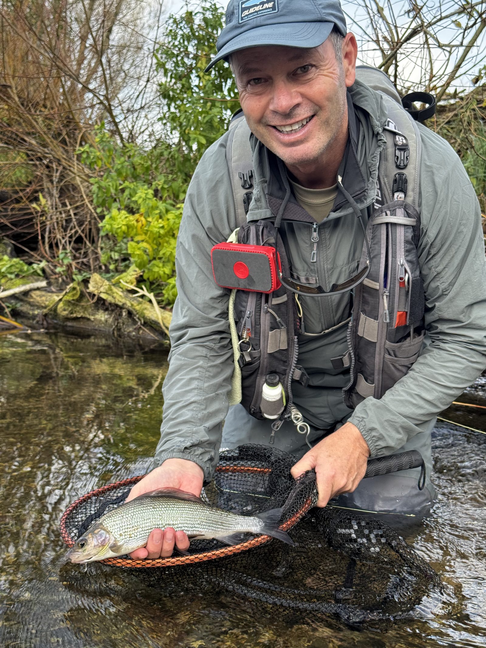 Smiling angler holding a grayling in a landing net on a winter river