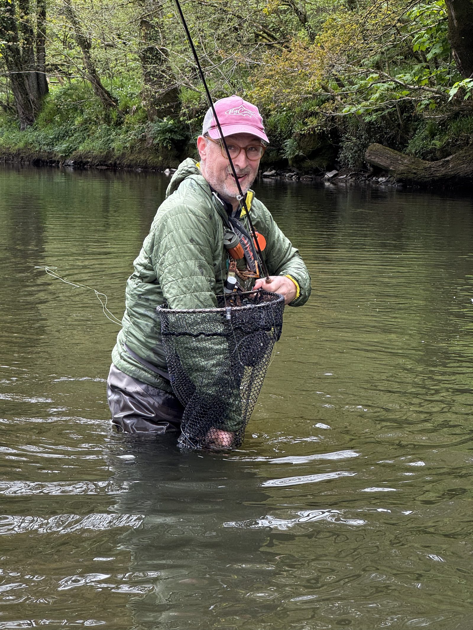 Fly angler standing in a river holding a landing net and looking towards the camera