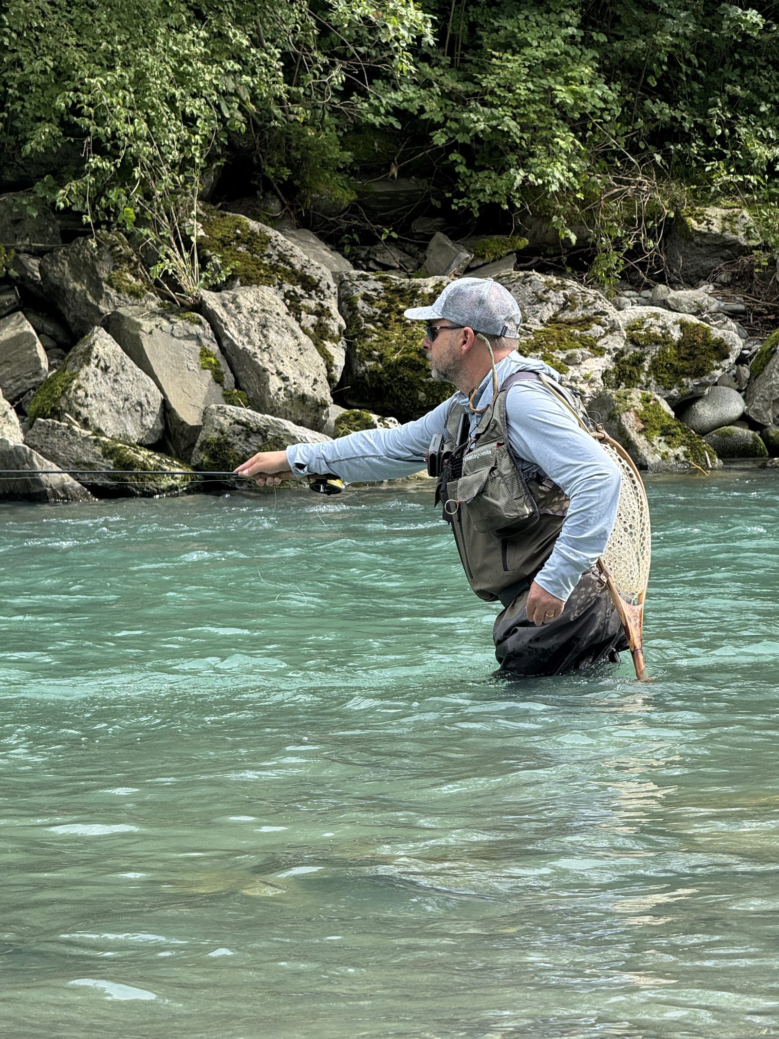 Fly angler delivering a parachute cast on a clear river while holding a landing net