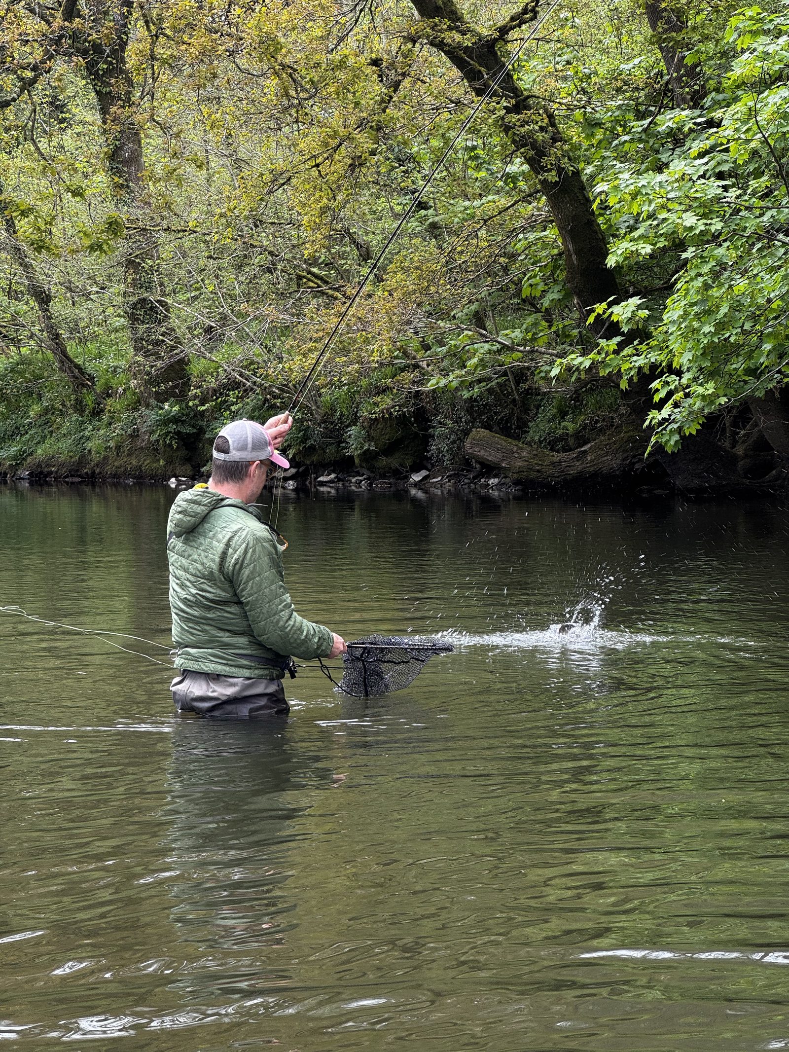 Fly angler playing a trout with a bend in the rod and a splash on a wooded river